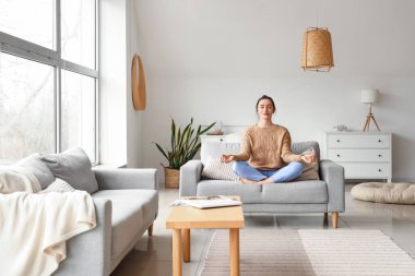 Evdeki kanepede meditasyon yapan güzel genç bir kadın.