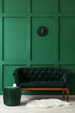 Yeşil duvarın yanında rahat bir kanepe ve puf.