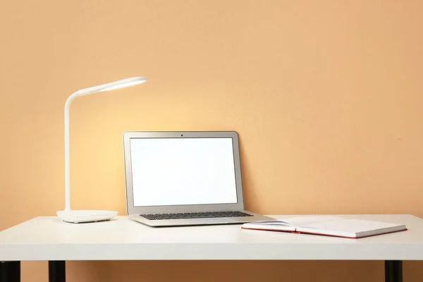 现代笔记本电脑和打开的笔记本在靠近彩墙的桌子上 — 图库照片