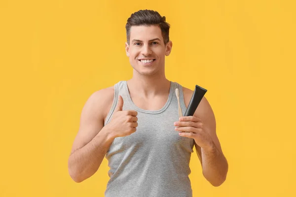 活性化された炭歯のペーストとブラシを持つハンサムな若い男は黄色の背景に親指アップを示しています — ストック写真