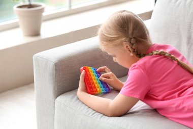 Kız kanepede uzanıyor ve Pop It ile oynuyor Aydınlık odada oyuncak, yakın plan