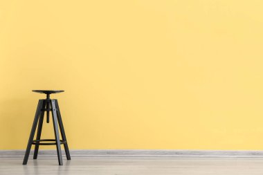 Sarı duvarın yanındaki modern tabure.