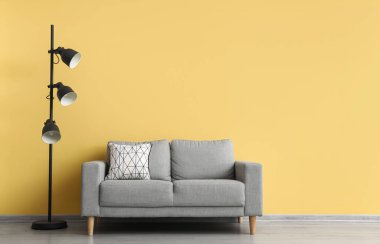 Modern lamba ve sarı duvarın yanındaki rahat kanepe.