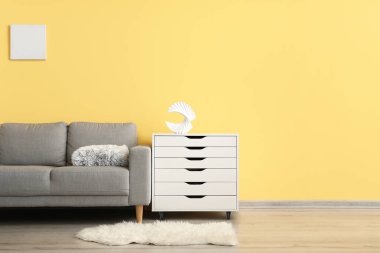 Modern çekmeceler ve sarı duvarın yanındaki rahat kanepe.