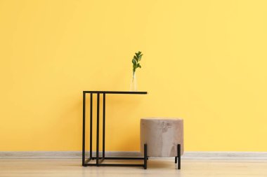 Sarı duvarın yanında puf olan şık bir masa.