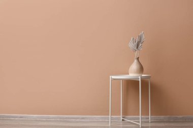 Bej duvarın yanındaki masada kurumuş çiçekli vazo.