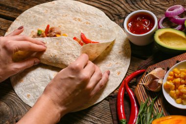 Ahşap arka planda etli lezzetli burrito hazırlayan kadın.
