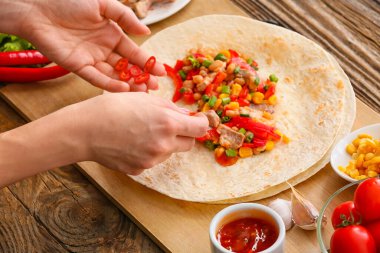 Ahşap arka planda etli lezzetli burrito hazırlayan kadın.