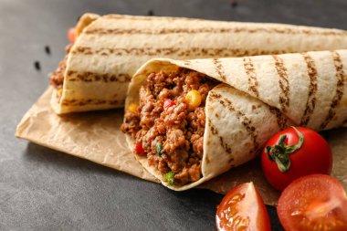 Lezzetli burrito ve domatesli parşömen koyu arka planda, yakın plan.