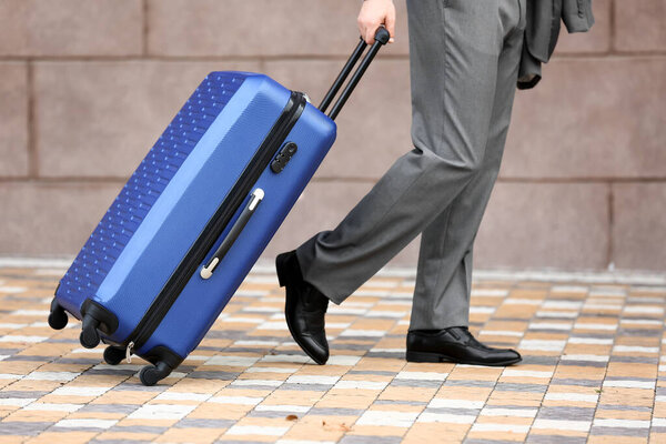 Young businessman with blue suitcase walking outdoors