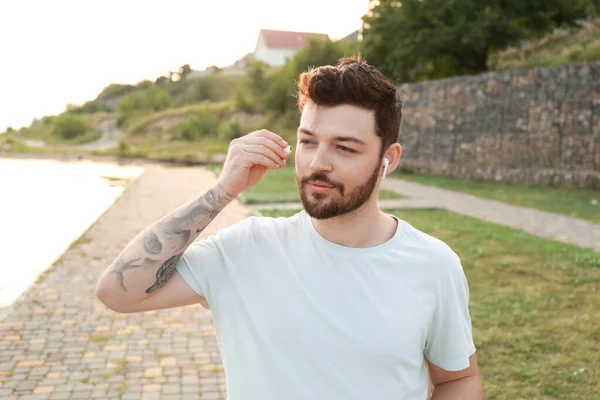 Hombre Guapo Poniéndose Auriculares Mientras Entrena Cerca Del Río —  Fotos de Stock