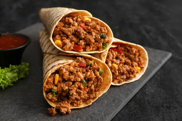 Lezzetli burritolar ve koyu arkaplanda sos tabağı, yakın plan.
