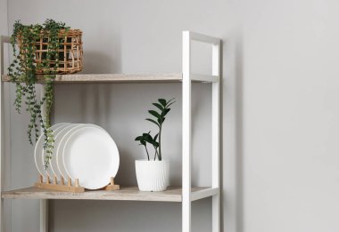 Mutfak duvarının yanında tabakları ve çiçekleri olan modern raf ünitesi.