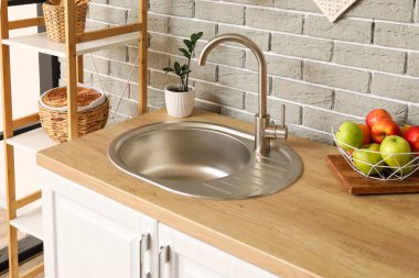 Mutfak tezgahında gri tuğla duvarın yanında elmalı gümüş lavabo ve kase.