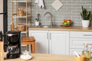 Mutfaktaki gri tuğla duvarın yanında lavabo ve raf ünitesi olan ahşap tezgah.