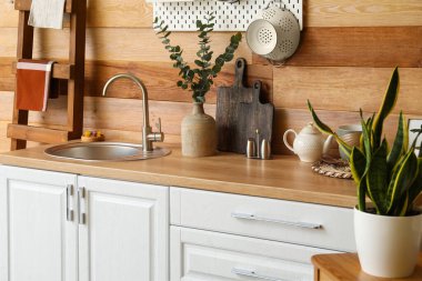 Ahşap duvarın yanında lavabo, vazo ve farklı yemek takımları olan modern bir tezgah.