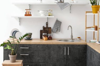 Lavabo, ev bitkisi ve beyaz duvarın yanında farklı yemek takımları olan ahşap tezgahlar.