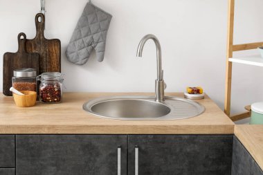 Beyaz duvarın yanında lavabosu, tahtaları ve kavanozları olan ahşap tezgahlar.