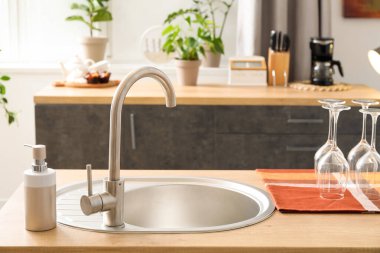 Gümüş lavabolu ahşap tezgah, bulaşık deterjanı ve mutfakta bardaklar.