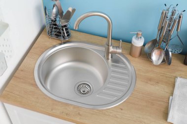 Mutfak duvarının yanında gümüş lavabo ve yemek takımı olan ahşap tezgah.