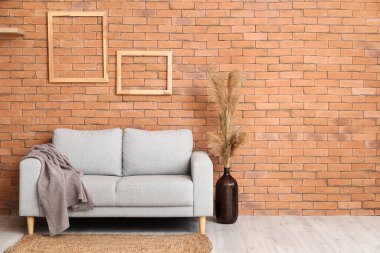 Rahat bir kanepe ve vazo. Tuğla duvarın yanında otlar var.