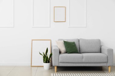 Yeni kanepe, boş posterler ve beyaz duvarın yanındaki çiçek.