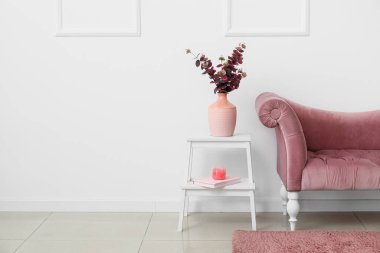 Beyaz duvarın yanındaki merdivende çiçekler olan yeni kanepe ve vazo.