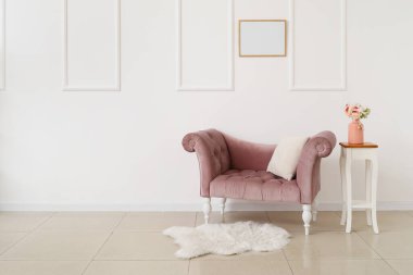 Beyaz duvarın yanındaki masada çiçekli yeni kanepe ve vazo.