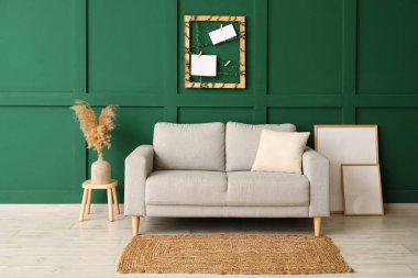 Yeni kanepe ve vazo. Yeşil duvarın yanındaki masada otlar var.