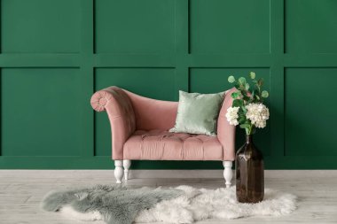 Yeşil duvarın yanında çiçekli yeni bir kanepe ve vazo.