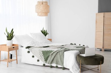 Rahat yatak, ev bitkileri ve dizüstü bilgisayar odada.