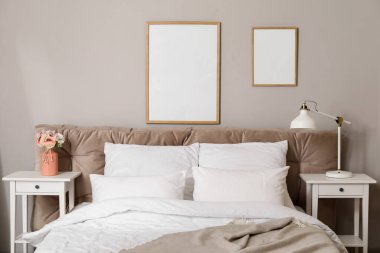 Rahat bir yatak, boş posterler ve ışık duvarının yanındaki masalar.