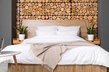 Rahat bir yatak ve ahşap duvarın yanında bitkiler.