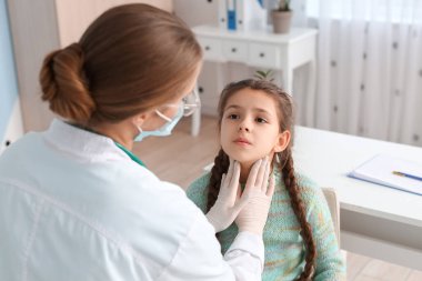 Doktor klinikte küçük kızın boynunu muayene ediyor.