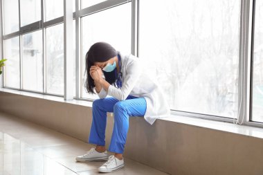 Klinikteki tıbbi maskeli endişeli kadın doktor.