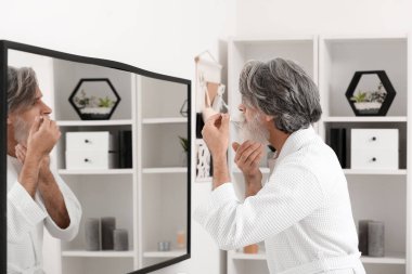 Olgun bir adam banyoda saç uzatmak için serum kullanıyor.