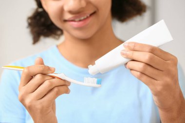 Afro-Amerikalı genç kız diş macununu banyodaki fırçaya sürüyor, yakın plan.