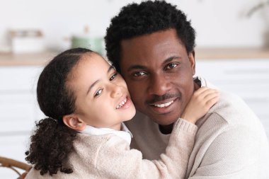 Mutlu Afro-Amerikalı adam ve küçük kızı evde sarılıyorlar.