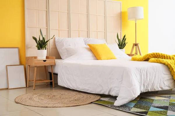 快適なベッド 折りたたみスクリーン ナイトスタンド 観葉植物やカラーウォールの近くの空白のポスター — ストック写真