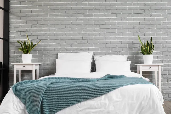 灰砖墙附近舒适的床 床头柜和室内植物 — 图库照片