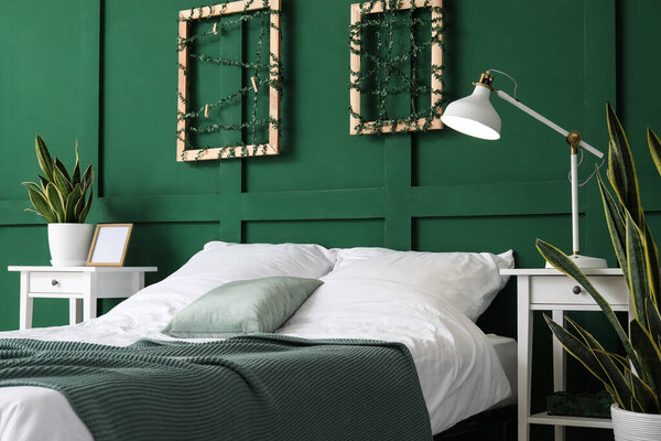 Интерьер стильной спальни с комнатными растениями возле зеленой стены