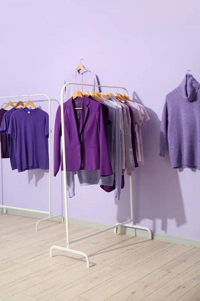 Racks with clothes in purple shades near lilac wall