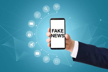 Mavi arkaplana karşı ekranda sahte haberlerle akıllı telefon tutan işadamının eli