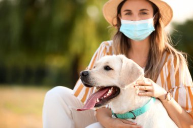 Sağlık maskeli bir kadın ve yaz günü dışarıda sevimli bir Labrador.