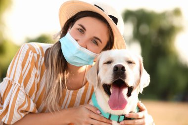 Sağlık maskeli bir kadın ve yaz günü dışarıda sevimli bir Labrador.