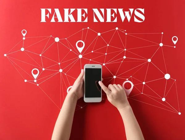 Çağdaş cep telefonlu çocuk elleri ve kırmızı arka planda sahte haber mesajı, üst görünüm