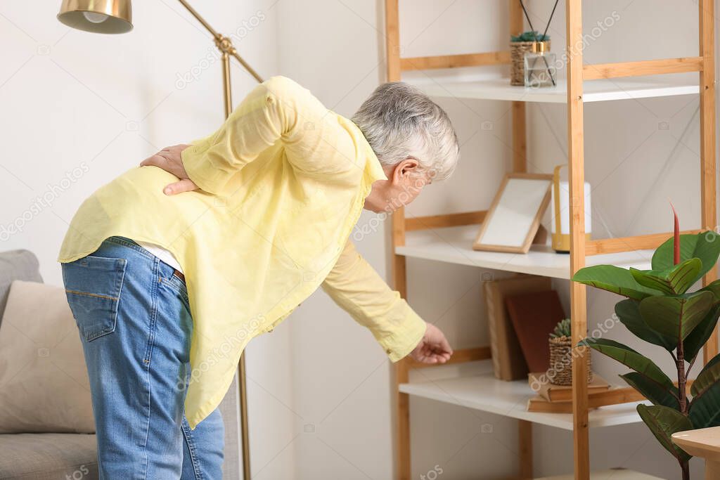 Senior woman with back pain taking book from shelf at home