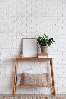 Güzel bir bitki ve beyaz tuğla duvarın yanındaki masada boş bir çerçeve.