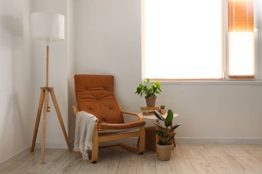 Oturma odasında rahat koltuk, lamba ve çiçek var.