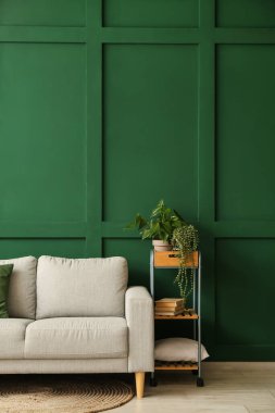 Yeşil duvarın yanında rahat bir kanepe ve bitkiler.